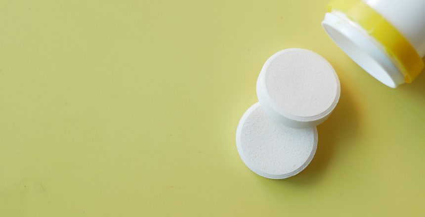 Effervescent soluble tablet pills on yellow .